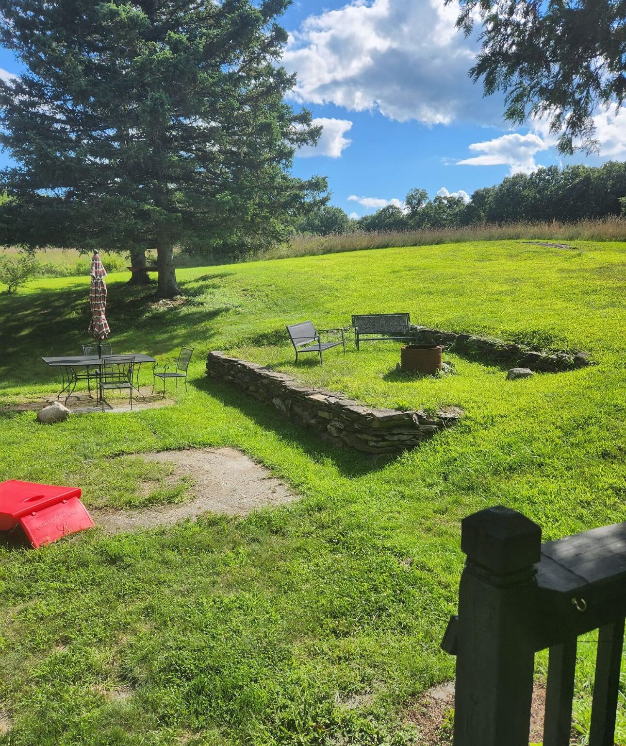 A grassy outdoor area with a stone wall, a bench, and a table with chairs.