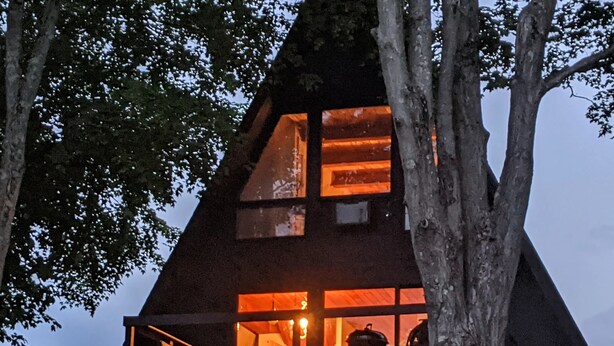 A cabin with a sloped roof, large windows, and a balcony with outdoor seating. - Cozy Rustic Cabin In The Hamlet Of Shushan NY. with  incredible views (shushan)