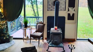 A cozy room with a wood-burning stove, a chair, a bench, and a Christmas tree. - Cozy Rustic Cabin In The Hamlet Of Shushan NY. with  incredible views (shushan)