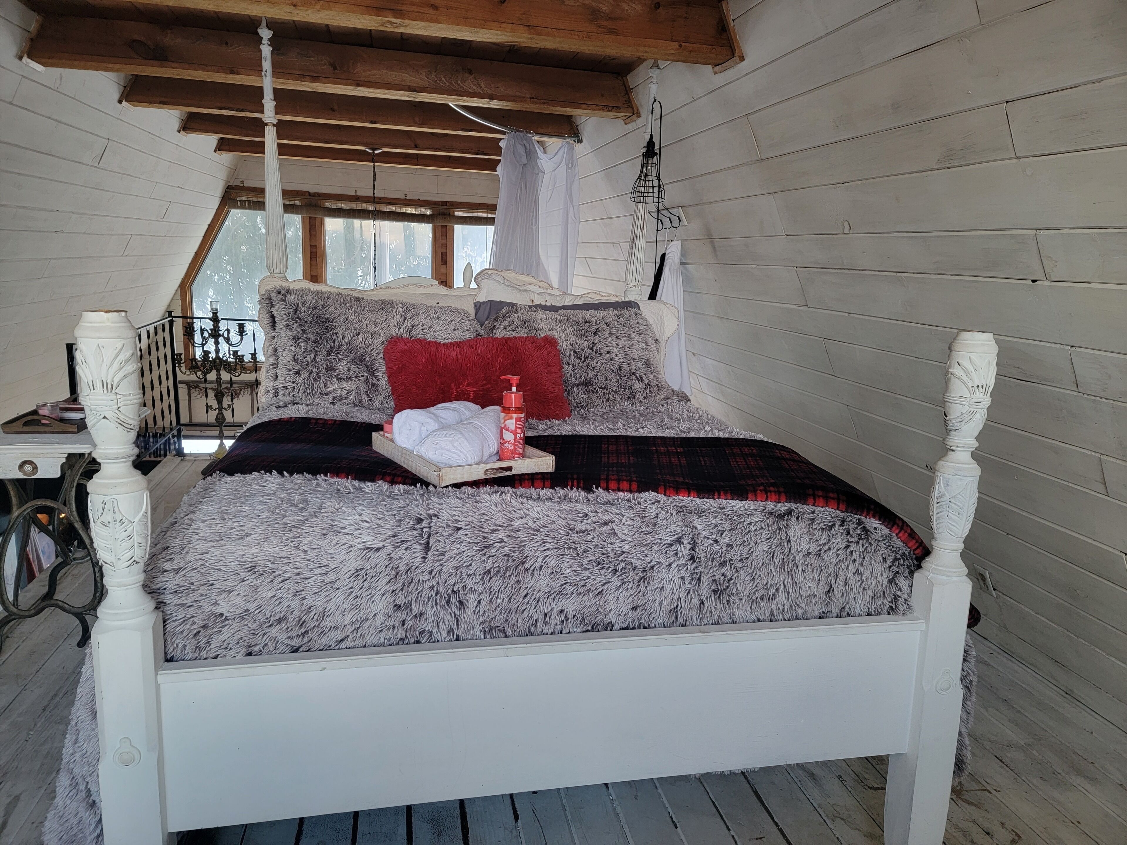 A bed with a fluffy gray and black blanket, a red pillow, and a bottle of lotion.
