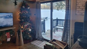 A cozy room with a decorated Christmas tree, a television, and a view of a snowy outdoor deck. - Cozy Rustic Cabin In The Hamlet Of Shushan NY. with  incredible views (shushan)