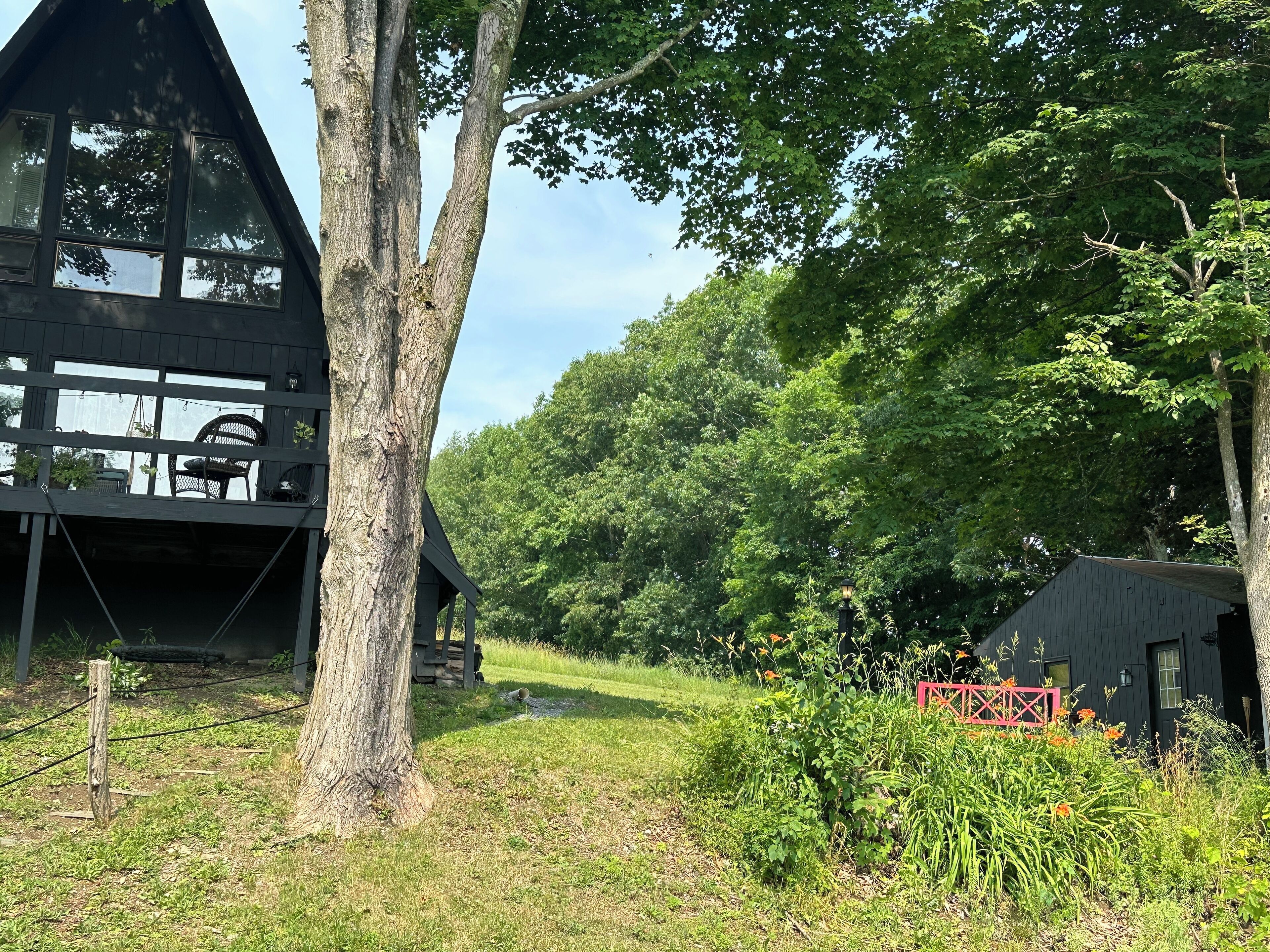 Une cabane dotée d’une terrasse, entourée d’arbres et d’un jardin.