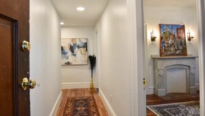 A hallway with a wooden floor, a painting on the wall, and a fireplace with wall sconces. - Beautiful Delightful 3BR Downtown Brunswick All King Beds (Brunswick)