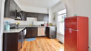 A modern kitchen with dark cabinets, stainless steel appliances, and a red refrigerator. - Beautiful Delightful 3BR Downtown Brunswick All King Beds (Brunswick)