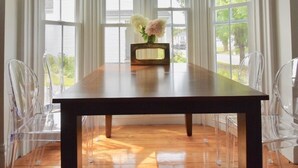 A dining area with a wooden table and clear chairs, large windows, and a vase with flowers. - Beautiful Delightful 3BR Downtown Brunswick All King Beds (Brunswick)