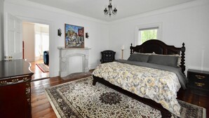 A bedroom with a large bed, a fireplace, a chandelier, and a painting on the wall. - Beautiful Delightful 3BR Downtown Brunswick All King Beds (Brunswick)