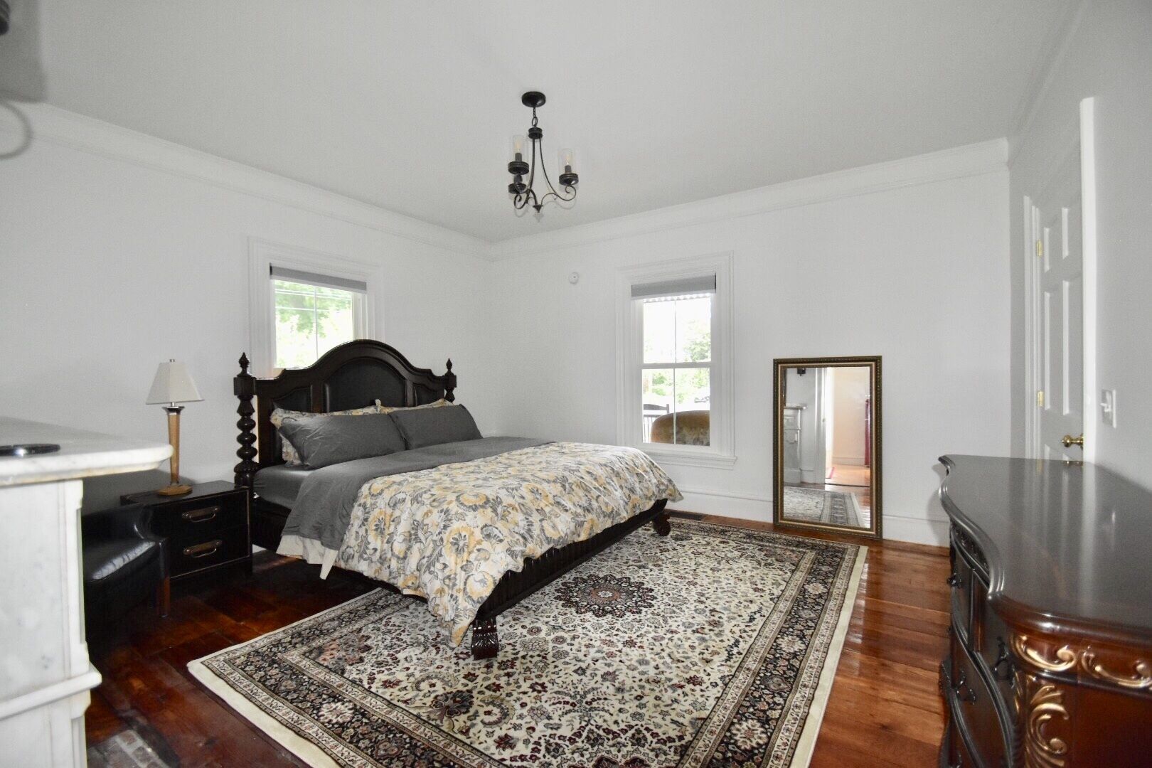 A bedroom with a large bed, a nightstand, a dresser, a chandelier, and a large mirror.