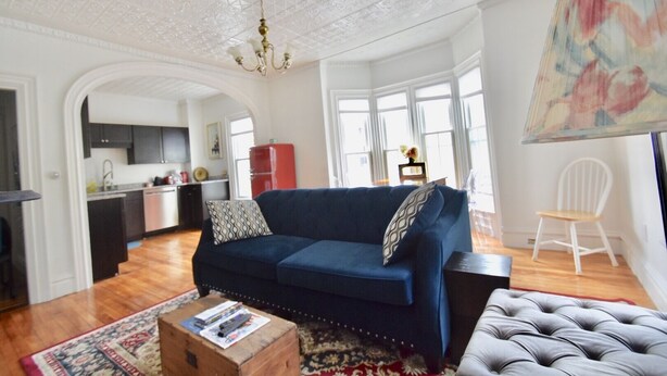 A spacious living room with a blue sofa, a white chair, a tufted ottoman, and a wooden coffee table. - Beautiful Delightful 3BR Downtown Brunswick All King Beds (Brunswick)