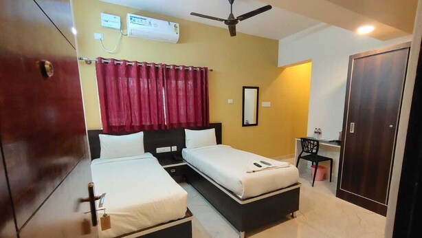 A hotel room with two beds, a desk, a chair, an air conditioning unit, and a wardrobe. - MK GRANDE (Bengaluru)