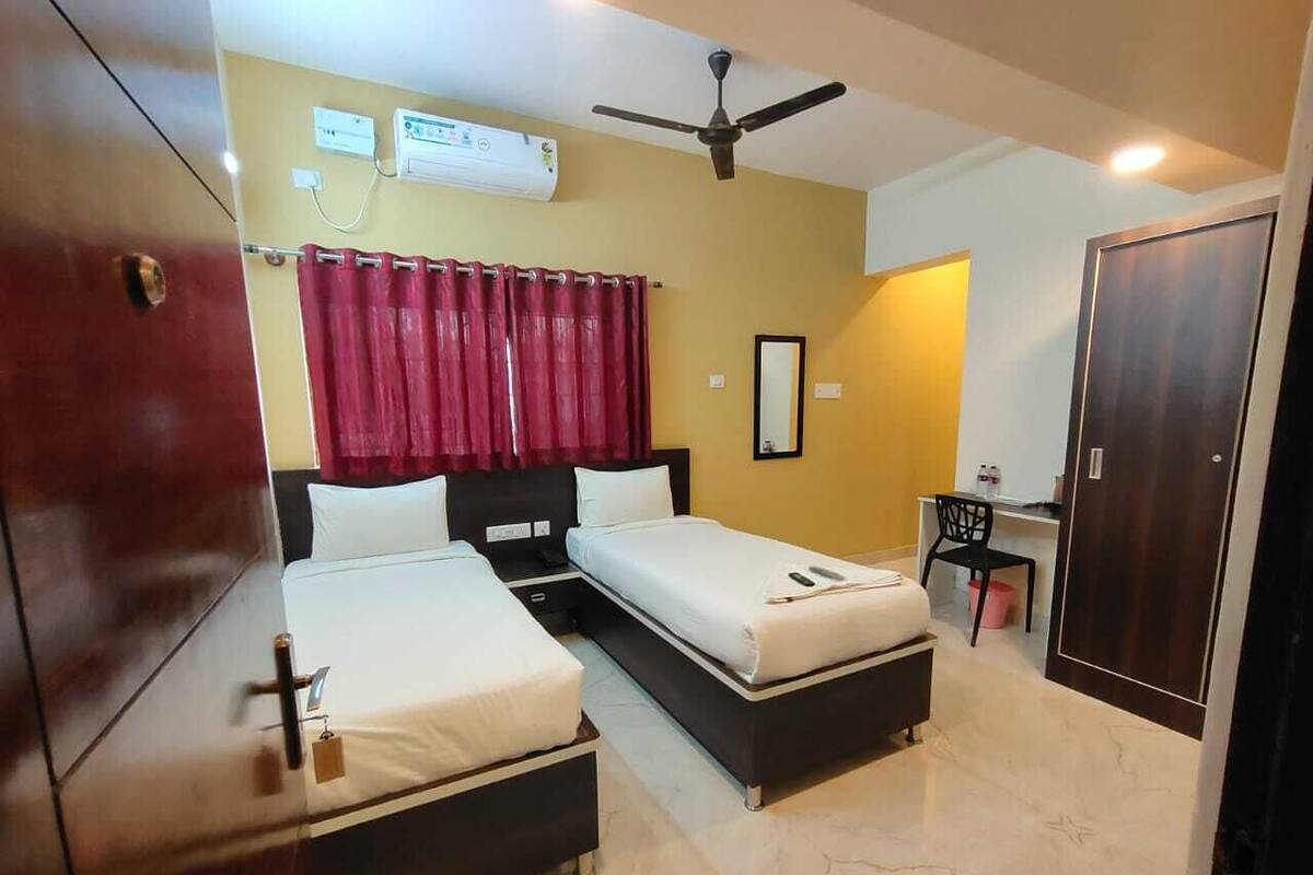 A hotel room with two beds, a desk, a chair, an air conditioning unit, and a wardrobe.