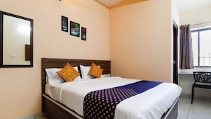 A neatly made bed with a dark headboard, white bedding, and patterned throw. There are three framed pictures on the wall above the bed. - MK GRANDE (Bengaluru)
