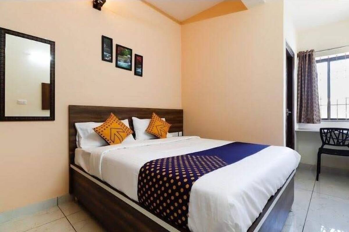 A neatly made bed with a dark headboard, white bedding, and patterned throw. There are three framed pictures on the wall above the bed.