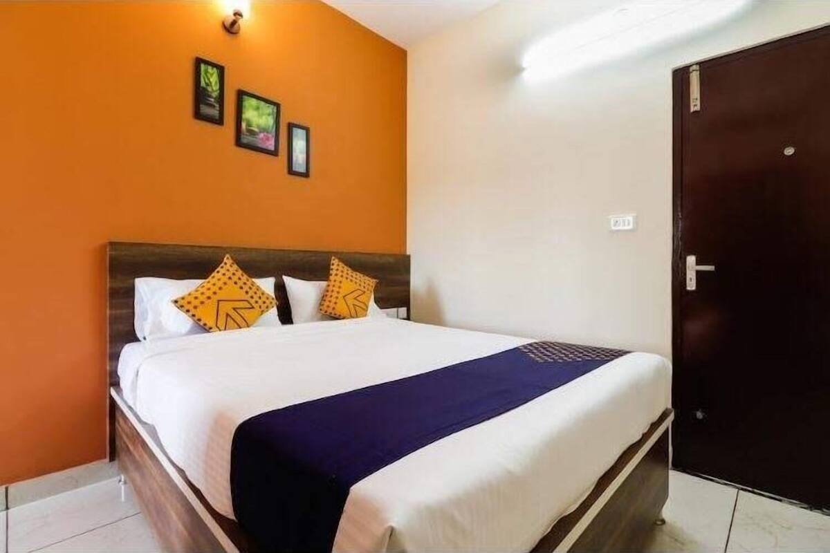 A hotel room with a bed, a dark wooden headboard, and a white wall with framed pictures.