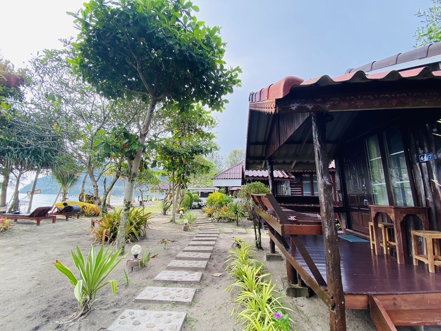 A wooden building with a porch, surrounded by tropical plants and a stone pathway.