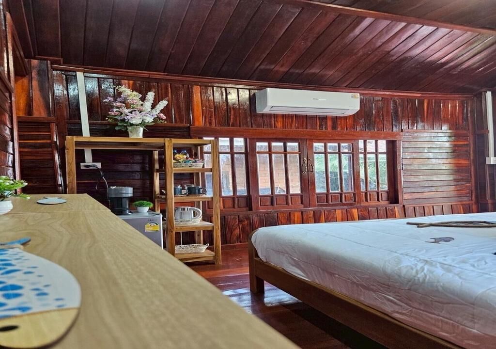 Une pièce en bois avec un lit, une table en bois, une étagère avec divers objets et une fenêtre donnant sur un paysage.