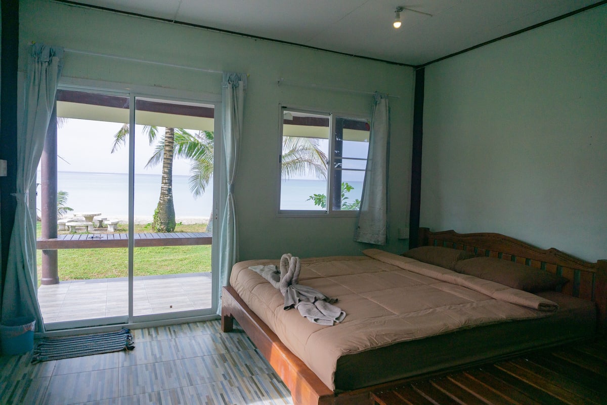 A bedroom with a large bed, a sliding glass door leading to a balcony, and a view of the ocean.