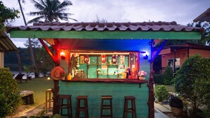 Un bar con fachada verde, taburetes de madera y techo de tejas.