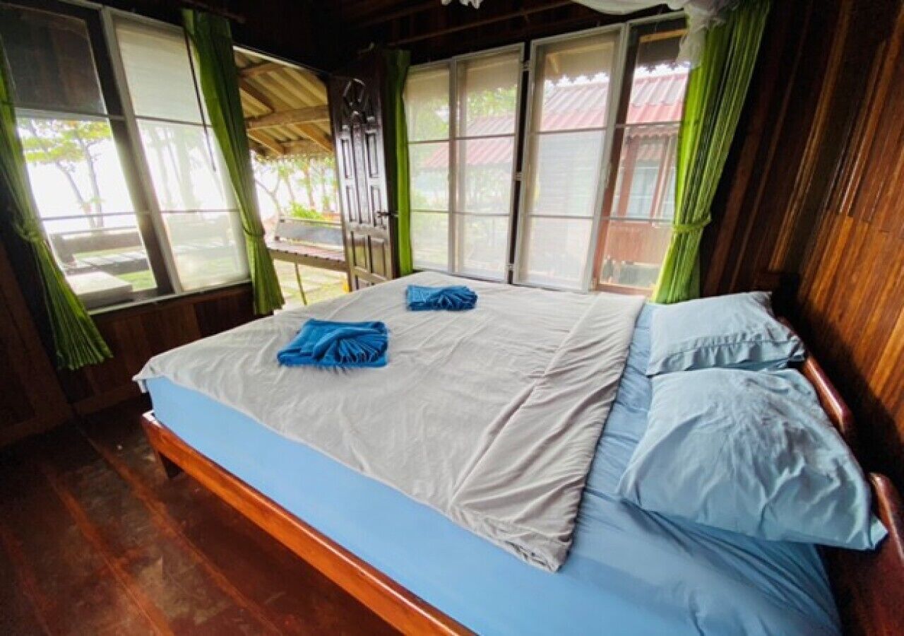 A room with a bed, wooden floor, and large windows with curtains.