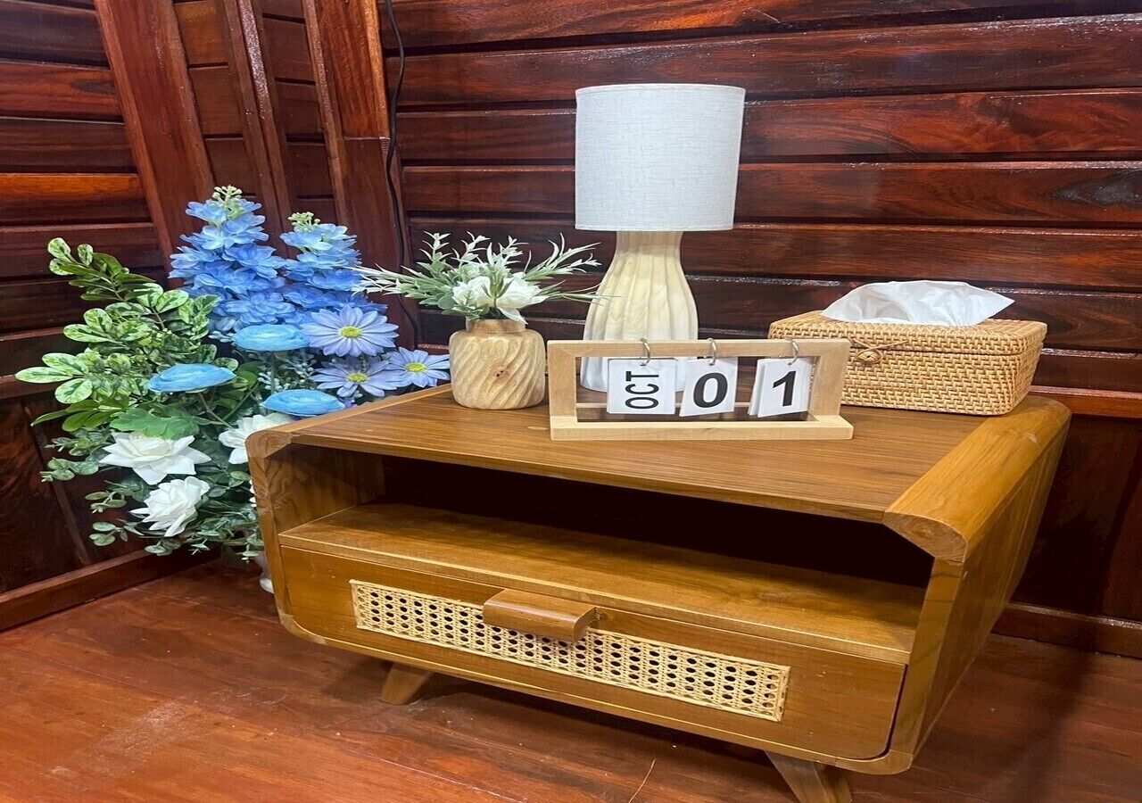 Ein Nachttisch aus Holz mit einer Lampe, einer Taschentuchbox und einer dekorativen Blumenanordnung.