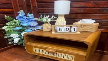 A wooden nightstand with a lamp, a tissue box, and a decorative arrangement of flowers.