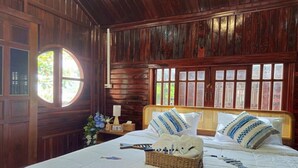 Una habitación de madera con una cama, un ventanal redondo y una mesita de noche con una lámpara.