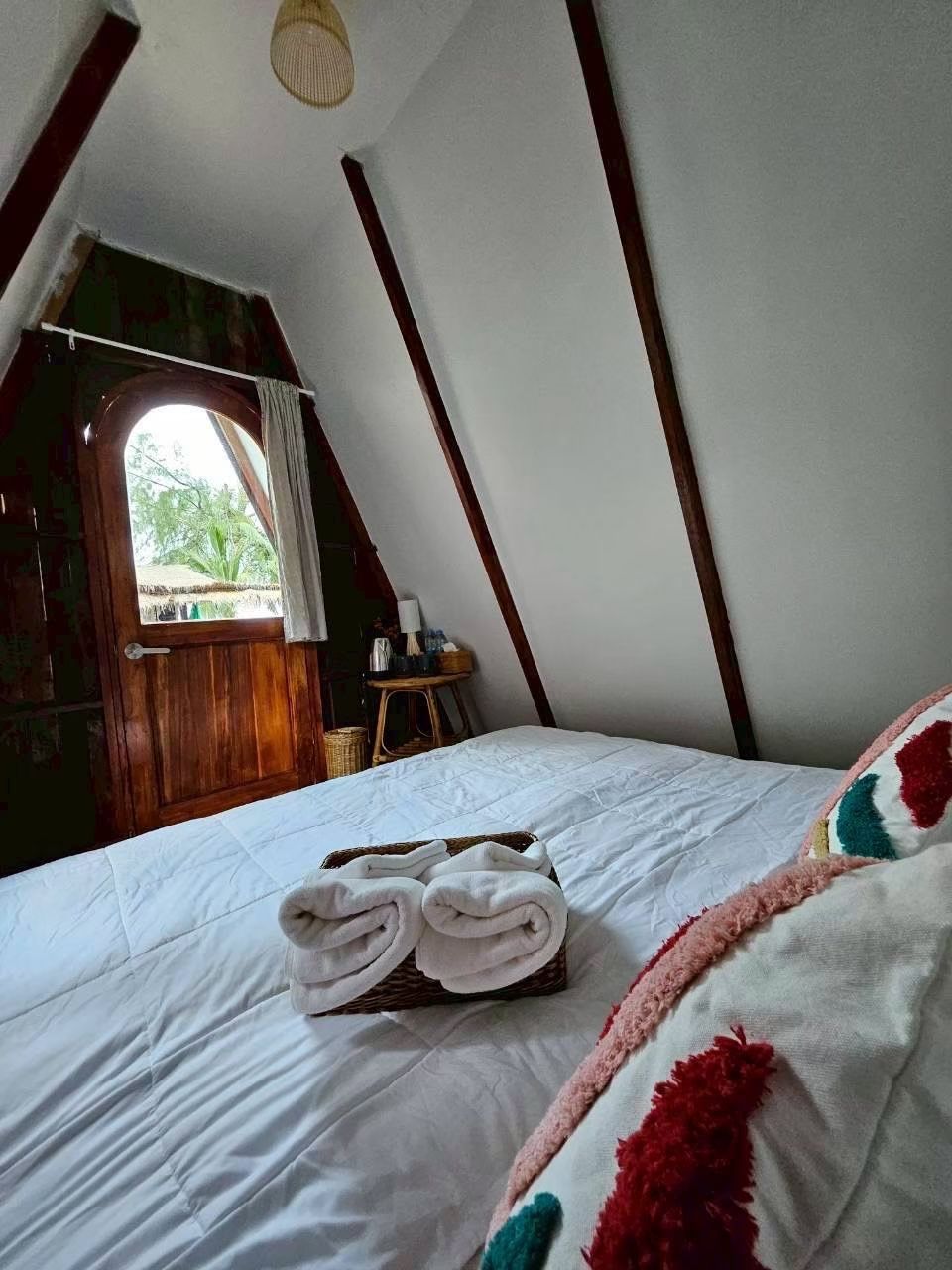 A cozy attic bedroom with a bed, a window, and a wooden door.