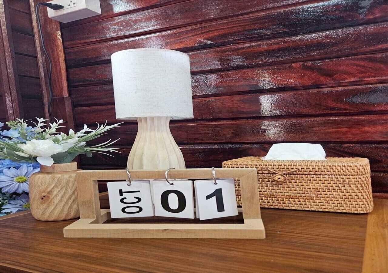 Una mesa de madera con una lámpara, una caja de pañuelos y un calendario de madera que muestra la fecha.