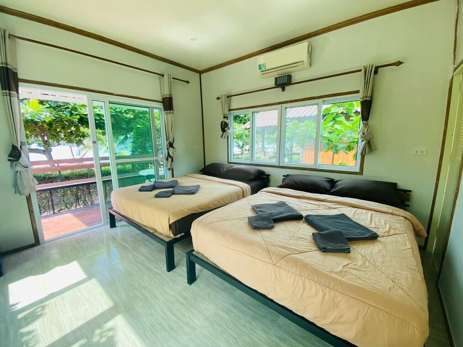 Una habitación con dos camas, ventilador de techo y ventanas amplias con cortinas.