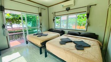 Una habitación con dos camas, ventilador de techo y ventanas amplias con cortinas.