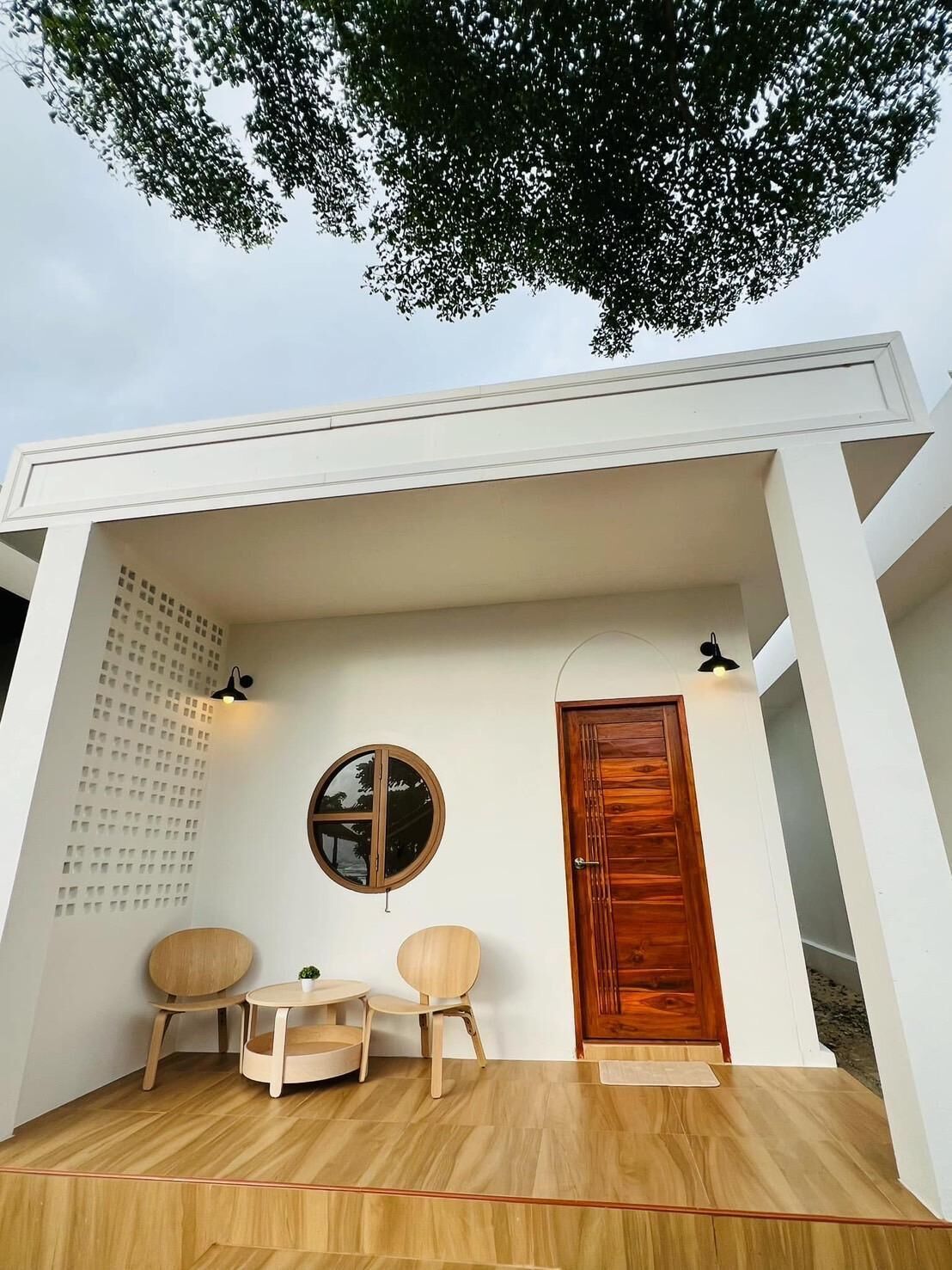 A modern outdoor seating area with a wooden table and chairs, a round mirror, and a wooden door.