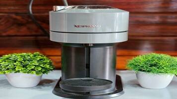 A Nespresso coffee machine on a white countertop with two small potted plants on either side.