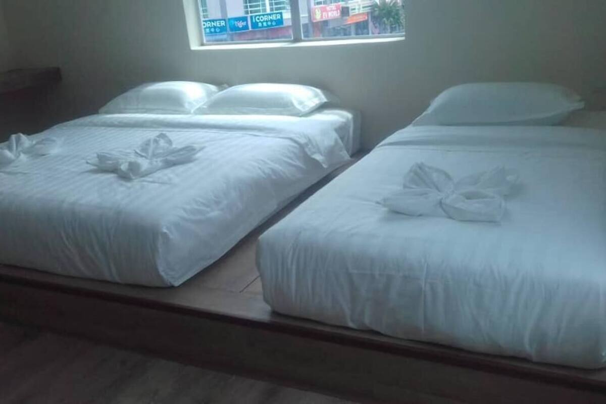 A room with two single beds, each with white linens and pillows, and a window with a view of a building outside.