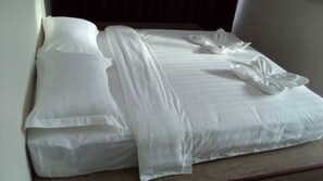 A neatly made bed with white linens and a decorative pillow arrangement. - Mass Hotel Mentakab (Mentakab)