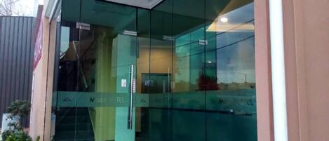 Entrada moderna de un edificio con puertas de vidrio y un letrero visible que dice "N25 TEL".
