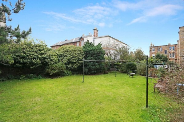 A backyard with a lawn, a wooden bench, and a metal fence.