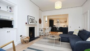Een moderne woonkamer met een donkerblauwe bank, een open haard en een eethoek met witte stoelen.