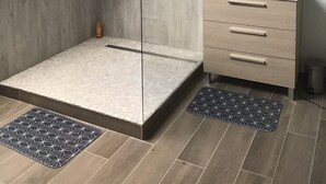 Ein modernes Badezimmer mit Dachfenster, einer Glaskabine zur Dusche, einem Holzwaschtisch und einem großen Spiegel.