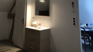 Ein Zimmer mit schrägen Deckenbalken, einer weißen Tür, einem Spiegel, einem Waschbecken und einem Tisch mit Stühlen.
