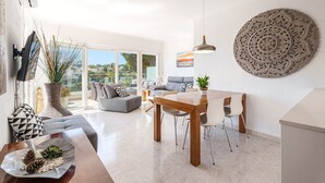 Een moderne woonkamer met een bank, eettafel en stoelen. Een groot raam biedt uitzicht op de omgeving.