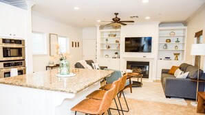 A modern kitchen with built-in appliances, a dining area with bar stools, a living room with a sofa and TV, and a fireplace. - ☀️HUGE Beach House!☀️3 blocks to BEACH🏖Ocean View🏝 3 BR/2.5BA (Oceanside)