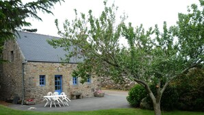 A stone building with a grey roof, a small porch with white chairs, and a tree in the foreground. - country holiday home - Goulien (Goulien)