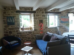 A stone-walled room with a sofa, a chair, a small table, and a window with a view of greenery.