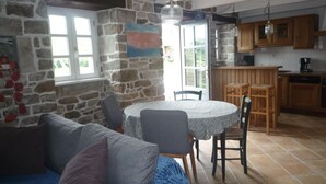 A cozy living room with a stone wall, a round dining table, and a kitchen area with wooden cabinets. - country holiday home - Goulien (Goulien)