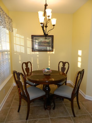 A dining room with a round table, four wooden chairs, a chandelier, and a framed picture on the wall.