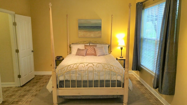A four-poster bed with a headboard, a bedside table with a lamp, and a window with curtains.