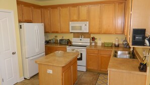 A kitchen with wooden cabinets, a white refrigerator, a microwave, a stove, and a sink. - Cozy and Convenient Furnished Townhome w/view (High Point)