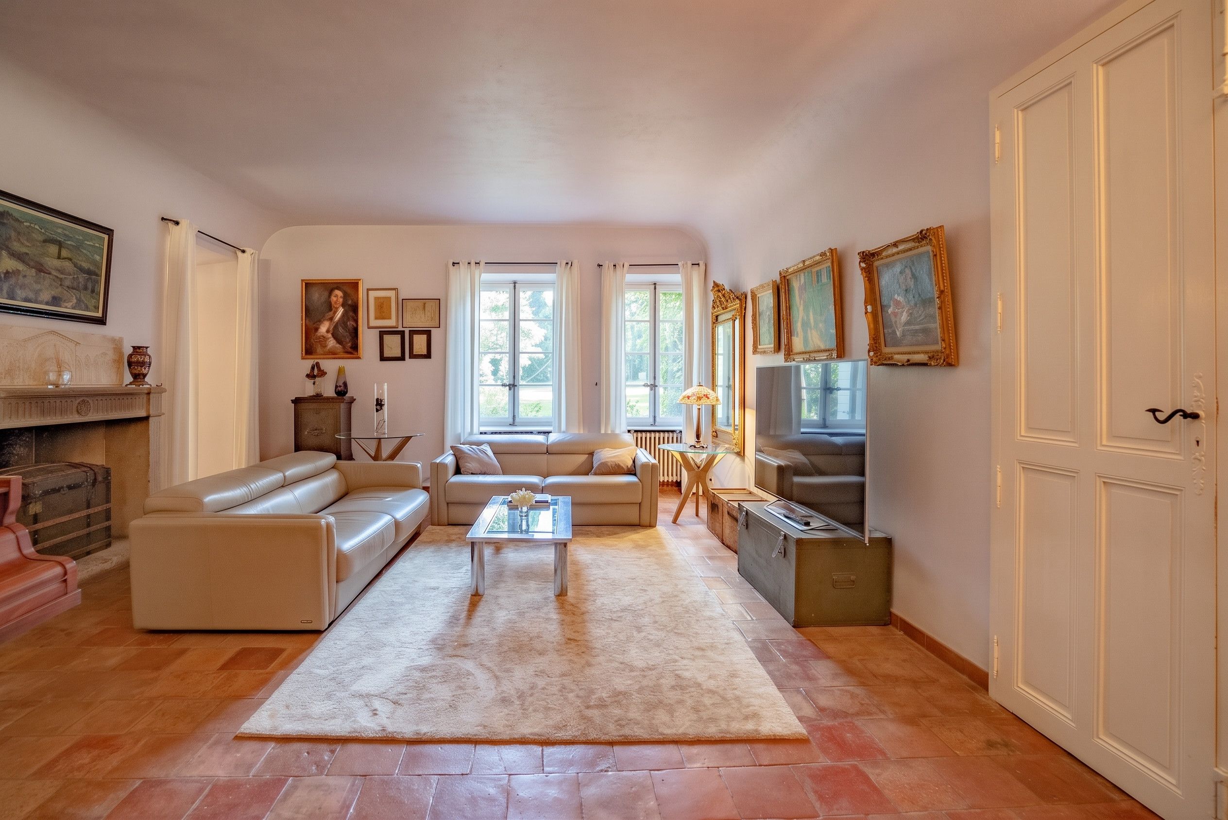 Un salon spacieux avec un canapé, une table basse et un téléviseur. Il y a deux fenêtres avec des rideaux, une cheminée et un meuble.