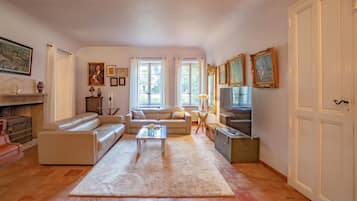 Un salon spacieux avec un canapé, une table basse et un téléviseur. Il y a deux fenêtres avec des rideaux, une cheminée et un meuble.
