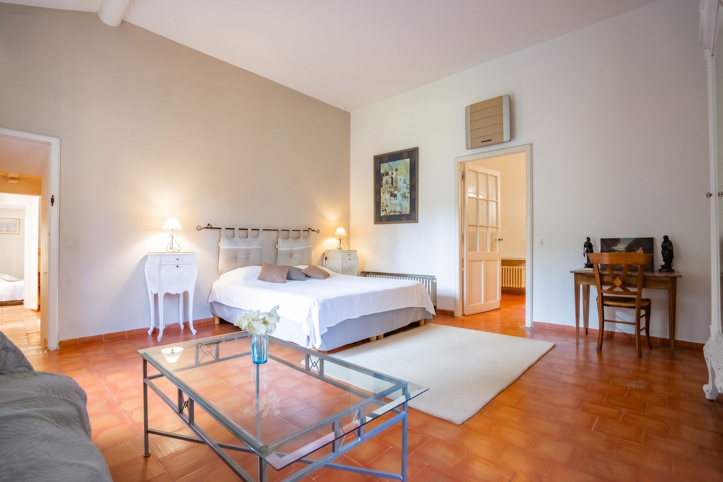 Ein Schlafzimmer mit einem Bett, Nachttischen, einem Glastisch, einer Heizung und einem Bild an der Wand.