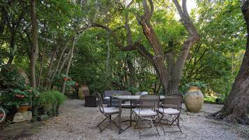 An outdoor patio with a table and chairs, surrounded by trees and potted plants.